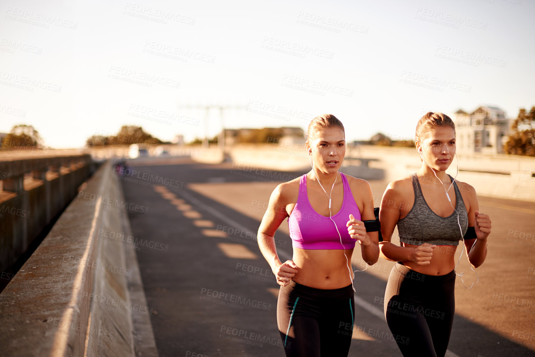 Buy stock photo Women, workout and bridge for running in city, streaming sound and team support with exercise. Urban town, fitness together and podcast for cardio sports, marathon training and earphones for twins