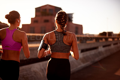 Buy stock photo Women, fitness and outdoor for running in city, streaming music and back support with exercise. Urban town, workout together and podcast for cardio sports, marathon training and earphones for audio