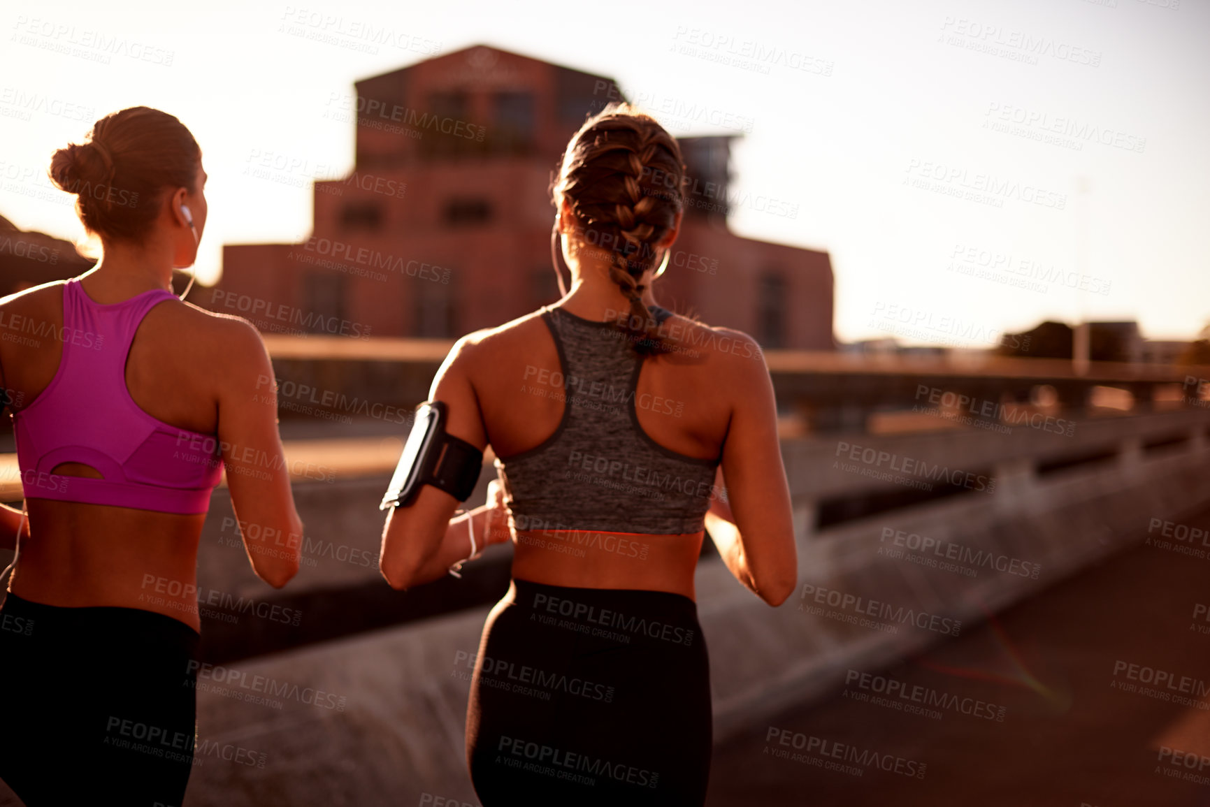 Buy stock photo Women, fitness and outdoor for running in city, streaming music and back support with exercise. Urban town, workout together and podcast for cardio sports, marathon training and earphones for audio