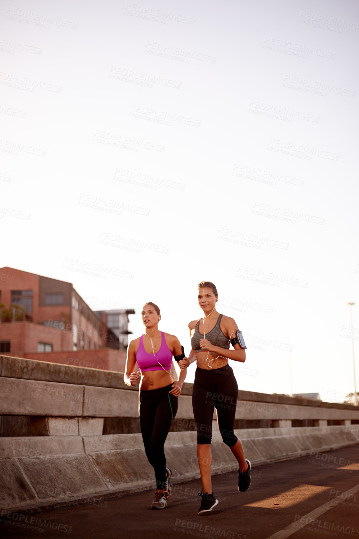 Buy stock photo Women, running and team in street with earphones, training and wearable tech on urban bridge. People, twins and sisters with exercise, streaming and smile for workout with mock up space in Germany