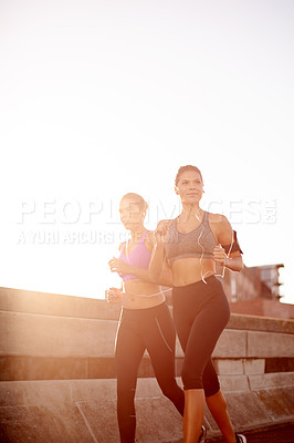 Buy stock photo Women, running and team with earphones on urban bridge, training and wearable tech in city. People, twins and sisters with exercise, streaming and smile for workout with mock up space in Germany