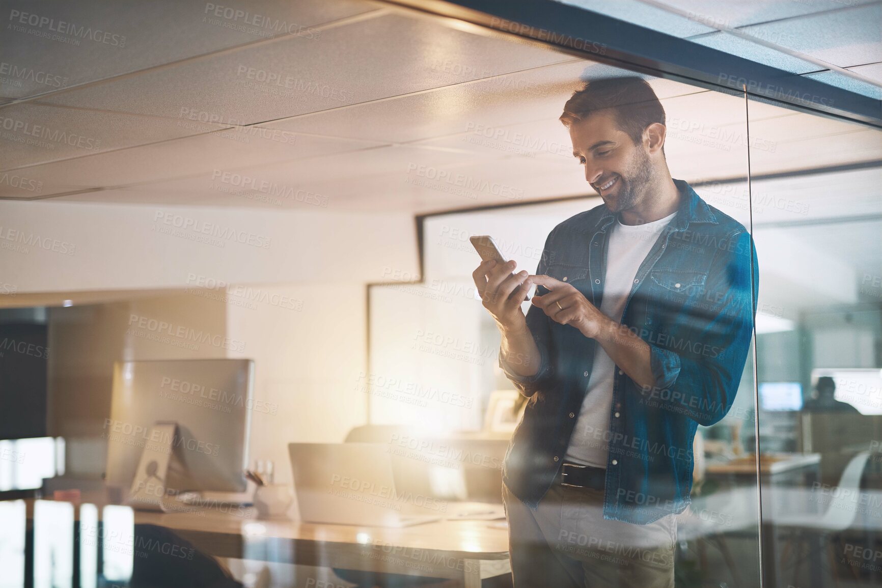 Buy stock photo Man, phone and texting in office, happy and overtime with update, reading and contact with app at night. Person, smartphone and check notification at startup, smile or web chat at creative agency
