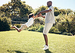 Cheerful african american dad swinging his son by the arms. Father playing with his son while spending time together outdoors at the park or in their backyard on a sunny day