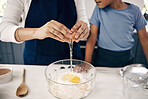 Closeup of female hands cracking a egg into a bowl while baking at home with her son. Woman adding ingredients to a glass bowl on the counter at home while baking with her child