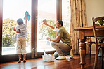 Young happy mixed race father and son washing windows together at home. Little hispanic boy helping his dad clean windows. Parent and child doing chores and cleaning a glass door. 