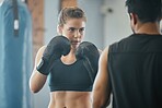 Boxing, exercise and training with a female boxer exercising with her fitness coach or personal trainer in the gym. Fighting, self defense and combat sport with a young woman and her workout partner