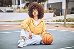 Young, fashionable and beautiful black woman basketball player or athlete with afro sitting on a court ground. Portrait of cool and edgy person in a casual outfit and funky fashion clothing outdoors