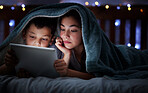 Happy caucasian family with two children using digital tablet lying under blanket in the dark at night with their faces illuminated by device screen light. Family of four reading online story or watching movie before bedtime