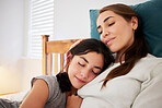 Loving caring mother sitting on a bed while her teenage daughter puts her head on her chest and falls asleep. Young caucasian mom bonding with her child at home embracing and showing love