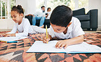 Little boy and girl drawing with colouring pencils lying on living room floor with their parents relaxing on couch. Little children sister and brother siblings colouring in during family time at home