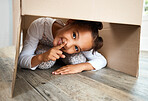 Portrait of a cute little hispanic girl playing with a cardboard box in a new apartment. Cute mixed race girl hiding in a box and smiling in a house. Relocation and moving day of big family