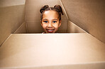 Portrait of a cute little hispanic girl playing with a cardboard box in a new apartment. Cute mixed race girl hiding in a box and smiling in a house. Relocation and moving day of big family