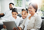 Happy mixed race smiling family of four bonding on a sofa while streaming movies on the internet using a digital tablet at home. Young couple looking cheerful with their daughter and son