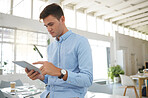 Young caucasian businessman working on a digital tablet alone in an office. One male boss holding and using social media on a digital tablet at work