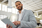 Portrait of a young happy mixed race businessman working on a digital tablet in an office. One hispanic male boss smiling and holding a digital tablet at work