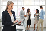 Mature happy caucasian businesswoman working on a digital tablet in an office. One confident female boss smiling and holding a digital tablet while in a meeting at work