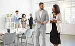 Mixed race businessman and african american businesswoman talking while using a digital tablet in an office with coworkers. Businesspeople working together