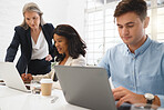 Three diverse businesspeople working together In an office at work. Mature businesswoman helping her colleagues with work on a computer. Young african american businesswoman using a laptop while getting help from a manager