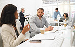 Young diverse colleagues talking while working on desktop computers together at a desk in an office at work. Young mixed race businessman talking to an african american businesswoman while working together