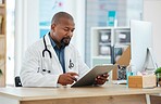 Mature african american doctor checking a patients chart. Focused gp reading a chart on a clipboard. Serious doctor reading a patients report. Professional physician reading a medical document