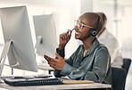 Happy young african american call centre telemarketing agent talking on a headset while working on a computer in an office. Confident friendly female consultant operating helpdesk for customer service and sales support