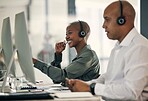 Happy young african american call centre telemarketing agent talking on a headset while working on a computer in an office alongside a colleague. Confident friendly female consultant operating helpdesk for customer service and sales support