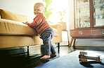 Baby boy, floor and learning to walk by couch for support, balance or infant muscle development in lounge. Young male child, portrait or stretching legs for walking by sofa in family home living room
