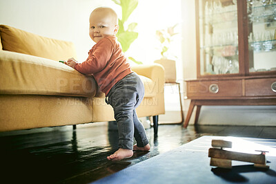 Buy stock photo Baby boy, floor and learning to walk by couch for support, balance or infant muscle development in lounge. Young male child, portrait or stretching legs for walking by sofa in family home living room