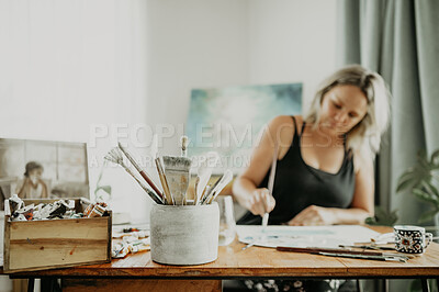 Buy stock photo Art, paintbrush and female artist painting in her home on canvas with creative career in studio. Creativity, equipment and young woman painter creating an artwork, illustration or design at her desk