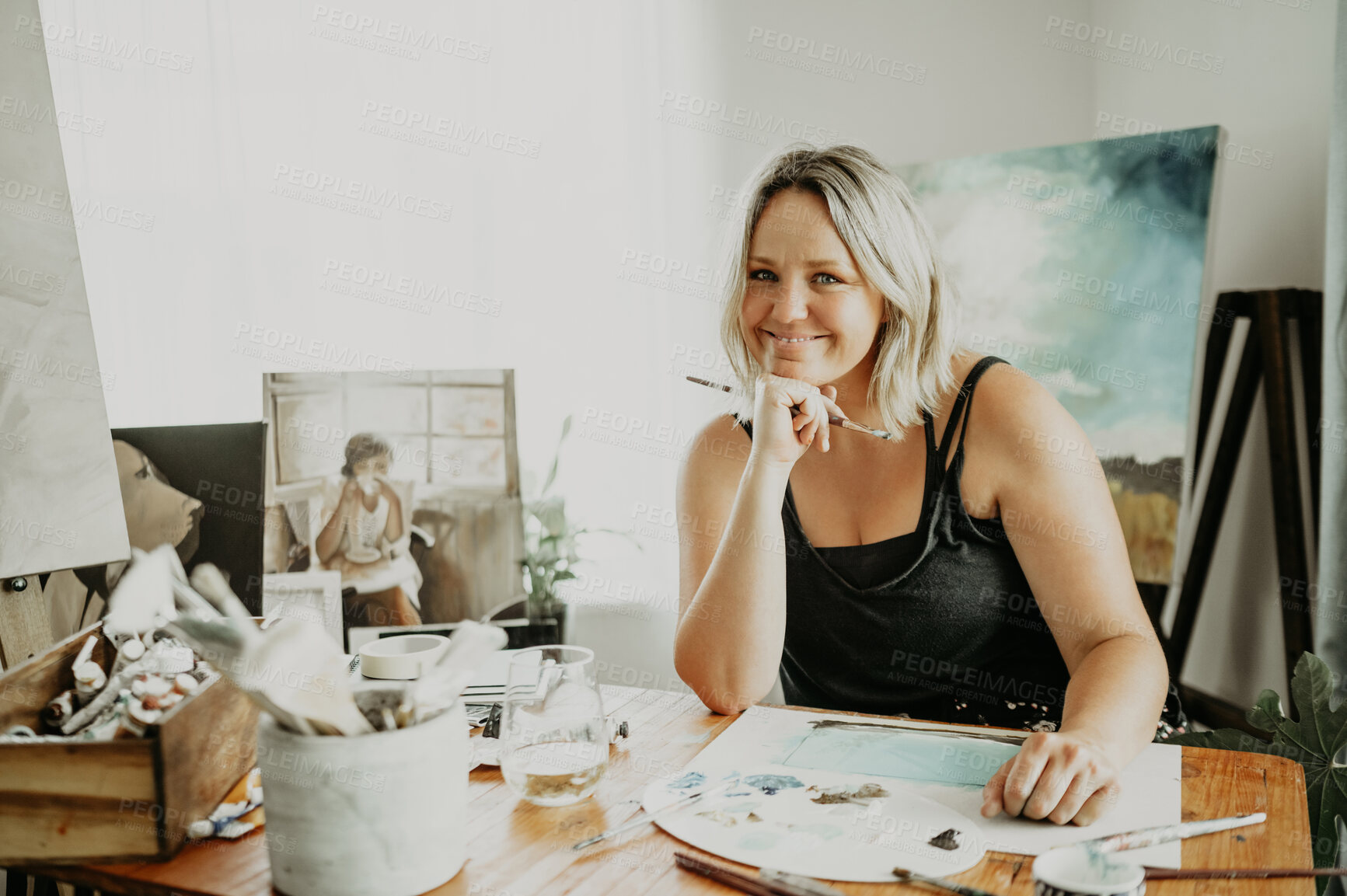 Buy stock photo Happy, painting and portrait of woman in studio at desk for drawing, illustration and artwork creation. Workshop, artist and female person with paintbrush, stationery and canvas for creative hobby