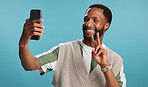 Selfie, peace sign or happy black man in studio with confidence, video call or fashion clothes. Smile, hand gesture or influencer on blue background for social media post, photo or vlogging update 