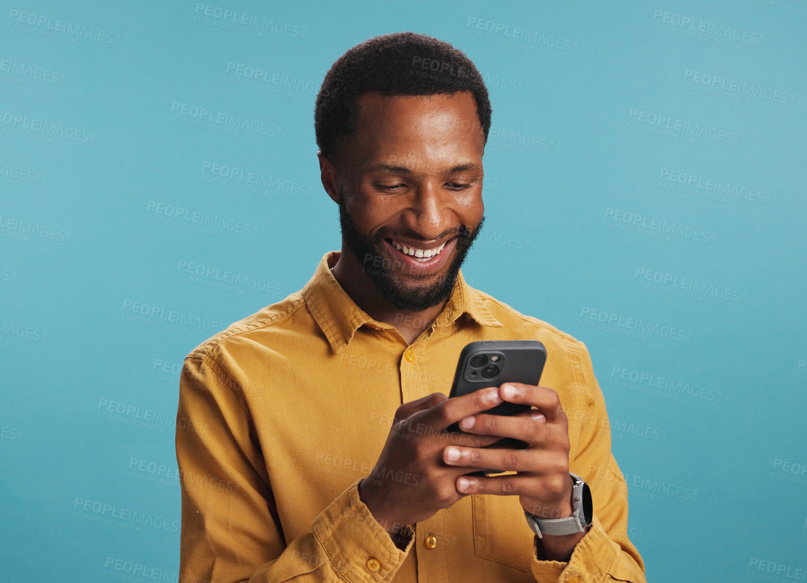 Buy stock photo Online, black man and happy with typing on smartphone in studio for text message, internet search and playing games. Mockup space, person and smile with phone for streaming service on blue background