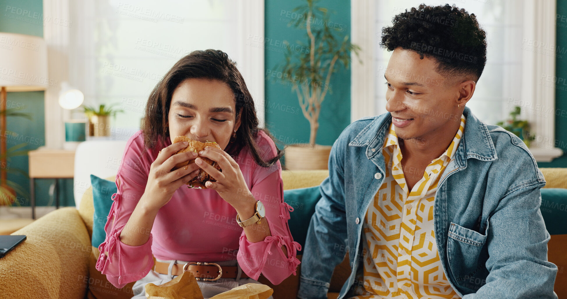 Buy stock photo Eating, couple and delicious food for woman, home and people with meal in living room, smile or takeaway. House, happy and man in relationship with hungry partner enjoying taste of burger in lounge