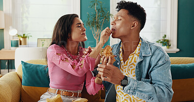 Buy stock photo Feeding, couple and delicious food for woman, home or people with meal in living room, smile or takeaway. House, happy and man in relationship with hungry partner enjoying taste of burger in lounge