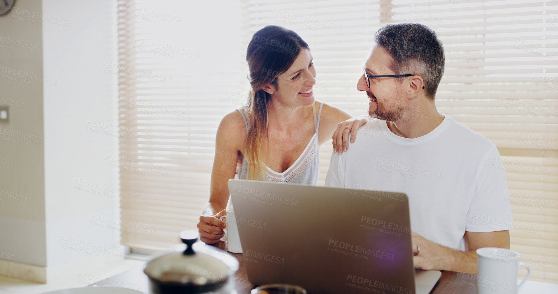 Buy stock photo Happy couple, talk and laptop in kitchen, breakfast and relax with coffee, streaming or social network in home. Mature man, woman and smile by computer, tea and love with funny memory at apartment