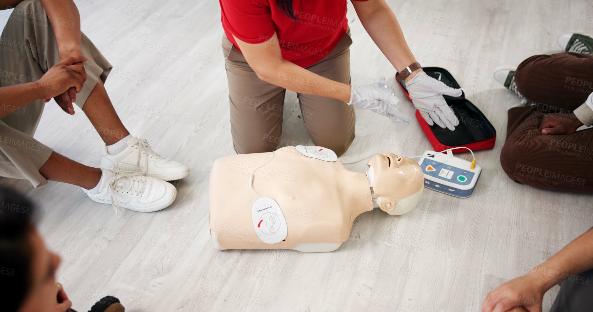 Buy stock photo Mannequin, teaching and workshop with people and defibrillator for first aid, cardiac arrest or safety protocol. Healthcare, medical simulation and heart rhythm rescue with paramedic course in office