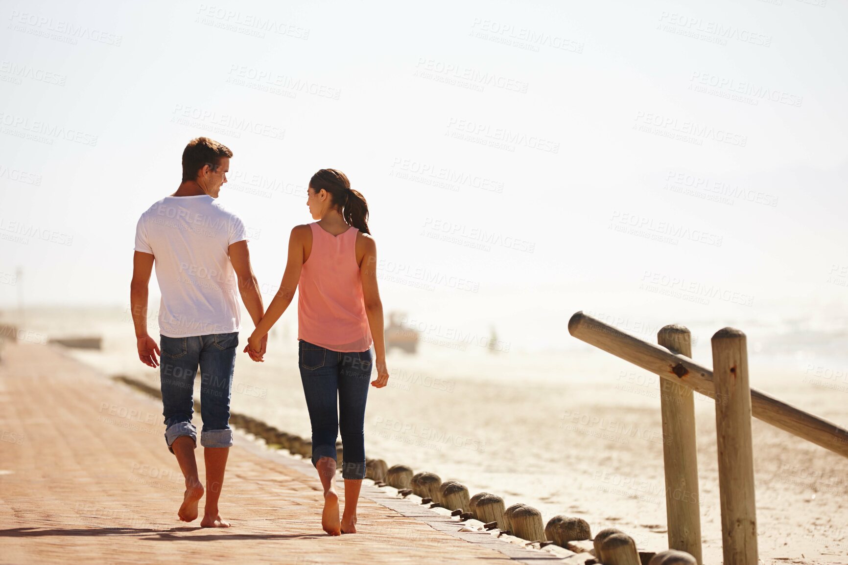 Buy stock photo Man, woman and holding hands for walk by the ocean, back view of romantic date and commitment with trust. Love, care and people outdoor for anniversary, bonding at beach with partner and travel