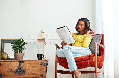 Buy stock photo Shot of a young woman relaxing at home with a magazine