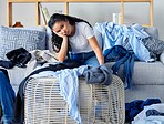 Frustrated, tired and woman with laundry in living room, clothing on floor and sofa, overwhelmed with workload. Stress, burnout and exhausted young housewife sitting on couch with messy apartment.