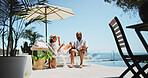 Couple, relax and champagne on vacation on patio, smile or conversation by ocean, celebration or valentines day. Mature people, man and woman with interracial love, drinks or holiday by sea in summer