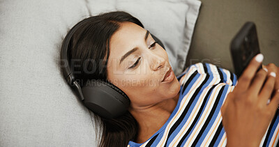 Buy stock photo Headphones, music and woman with phone on sofa for social media, streaming subscription and radio. Happy, chill and girl on smartphone listening to audio, playlist and podcast to relax in living room