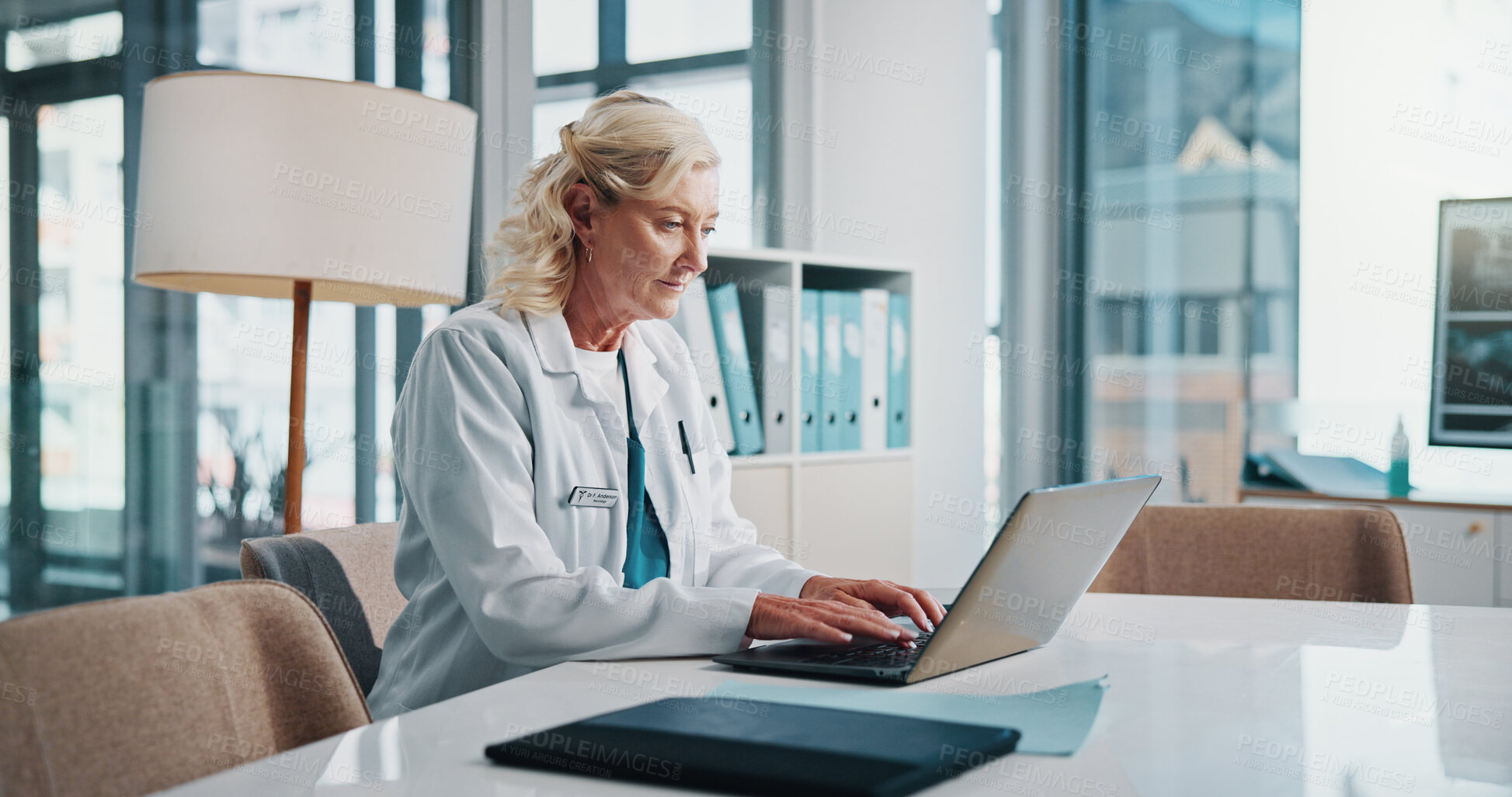 Buy stock photo Doctor, laptop and medical with woman at desk in office of hospital for diagnosis, planning or research. Computer, healthcare and typing with mature medicine professional in clinic to update records