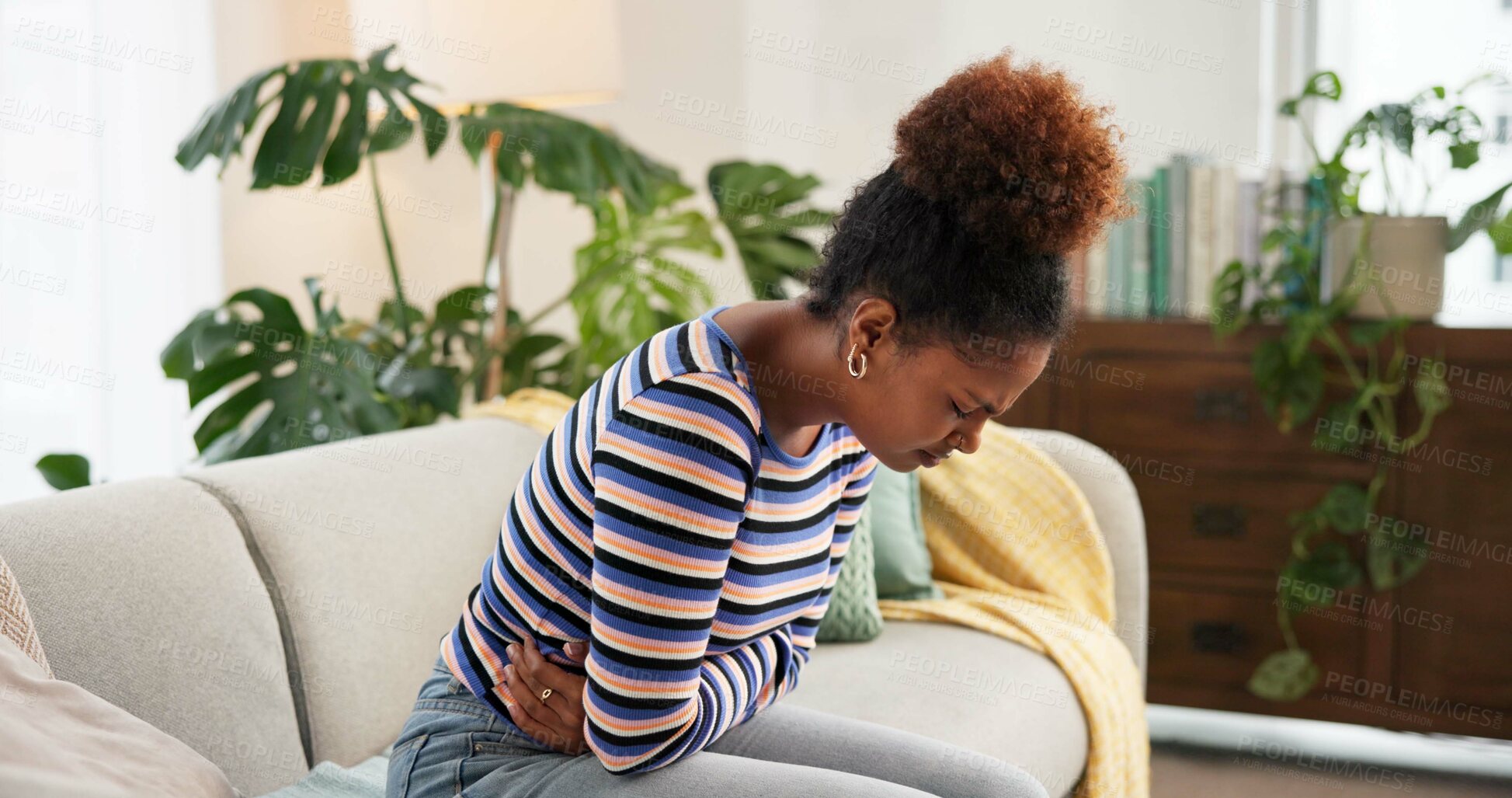 Buy stock photo African, woman and stomach pain on couch at house with period cramps, digestion problem and bloated. Female person, abdomen and endometriosis crisis with gut health, uncomfortable and menstruation