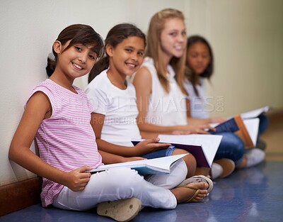 Buy stock photo Girl, students and portrait of friends with books sitting at school in hallway for education or learning. Group of young kids or children smile with textbooks on corridor floor outside classroom