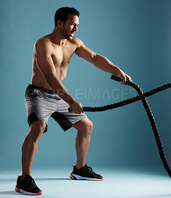 Buy stock photo Fitness, studio and man with battle ropes for workout, exercise and body wellness. Muscle, shirtless bodybuilder and equipment for strength, power training and cardio endurance on blue background