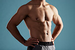 Closeup young mixed race man standing shirtless in studio isolated against a blue background. Unrecognizable muscular male athlete standing with his hands on his hips during a break from his workout