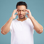 Handsome young mixed race man suffering from a headache with his eyes closed while standing in studio isolated against a blue background. Hispanic male struggling with a migraine and feeling sick