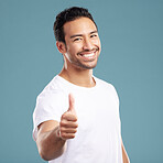 Handsome young mixed race man giving thumbs up while standing in studio isolated against a blue background. Hispanic male showing support or appreciation. Backing or endorsing a product or company