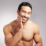 Handsome young mixed race man touching his face and posing shirtless isolated in studio against a grey background. Hispanic well groomed male looking confident and happy with his daily skincare regime