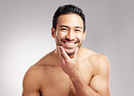 Handsome young mixed race man touching his face and posing shirtless isolated in studio against a grey background. Hispanic well groomed male looking confident and happy with his daily skincare regime